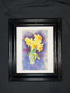 Daffodils (Original Watercolor Painting): A framed artwork featuring yellow and orange daffodils in a glass vase, set against a purple-blue background and displayed on black fabric.